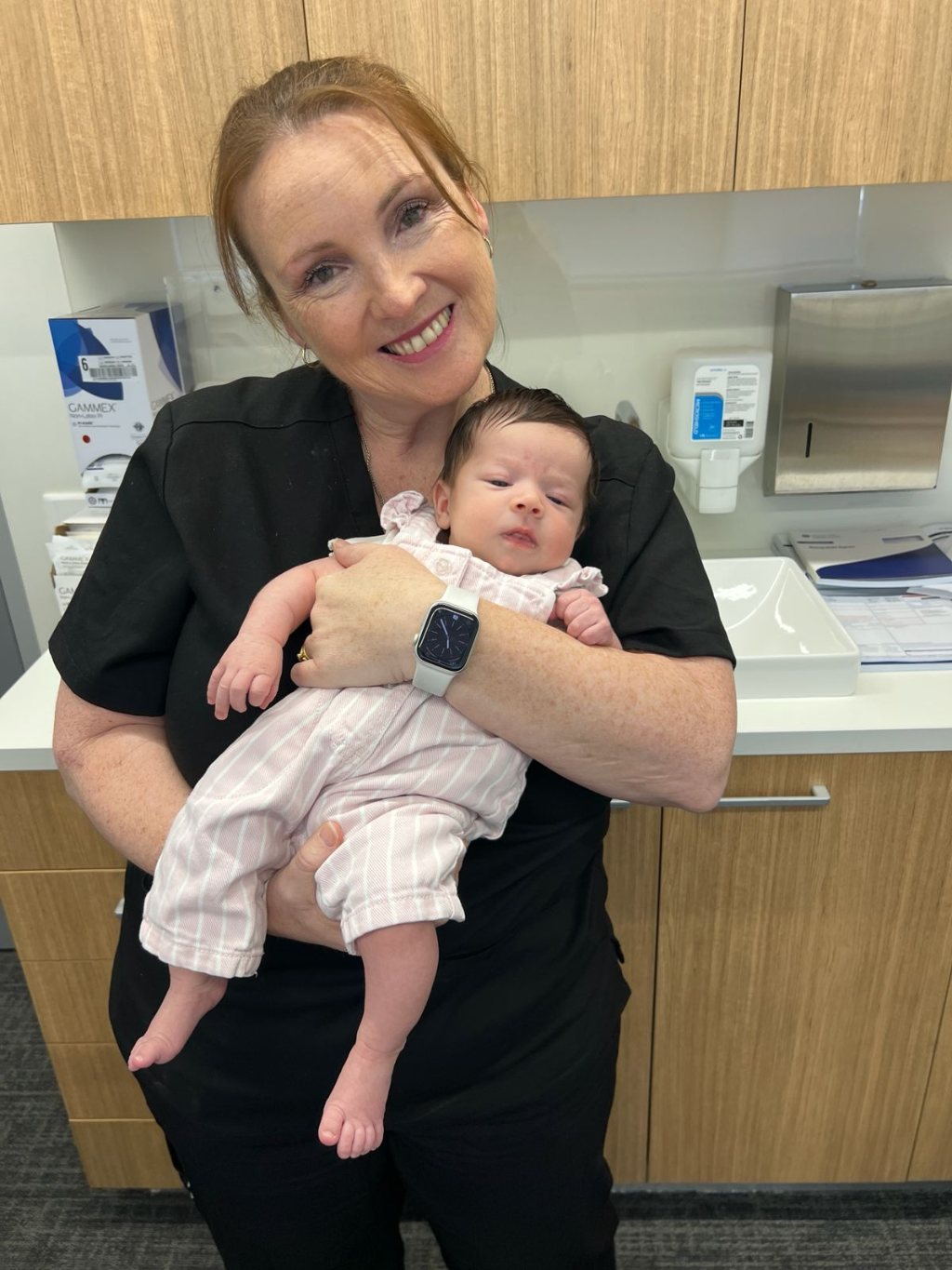 Rebecca holding a newborn baby, smiling at the camera